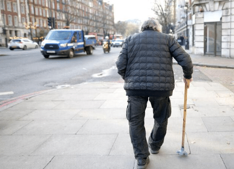 uomo anziano di spalle con gambe vare che cammina con il bastone